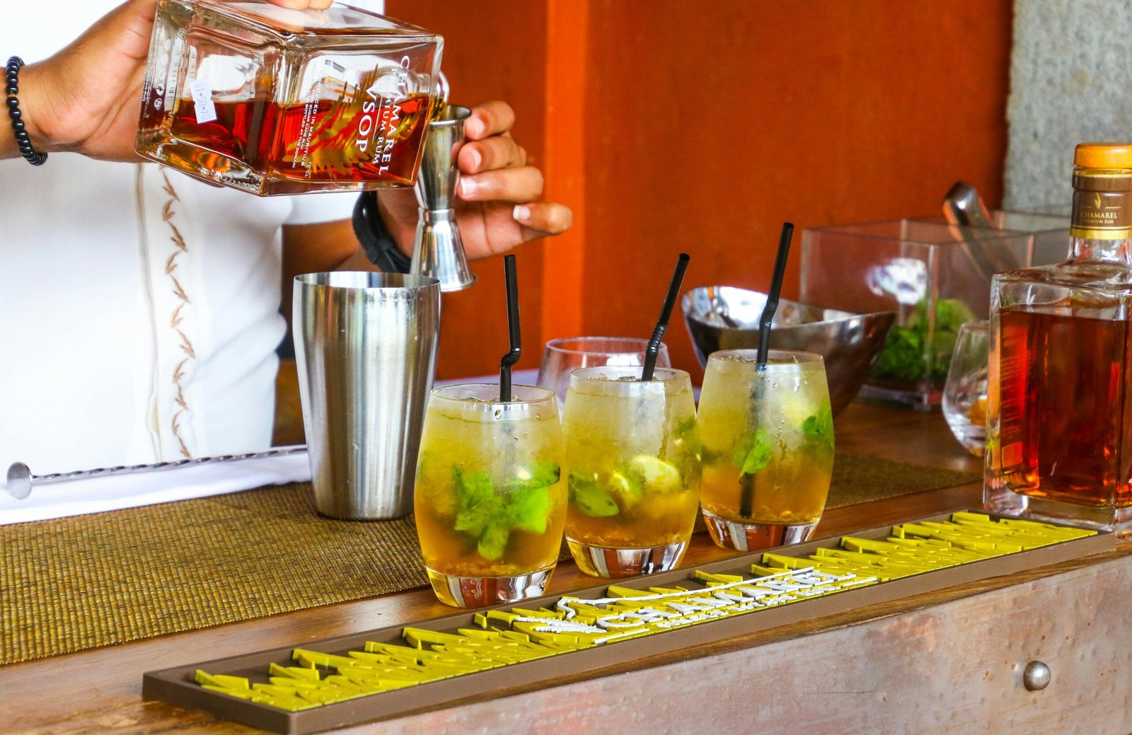 Bartender pouring rum into cocktail glasses at a vibrant bar setting.